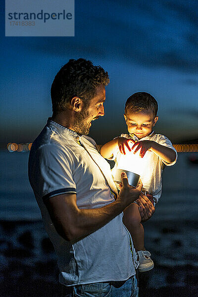 Aufgeregt trägt der Vater seinen Sohn mit Beleuchtungsausrüstung am Strand