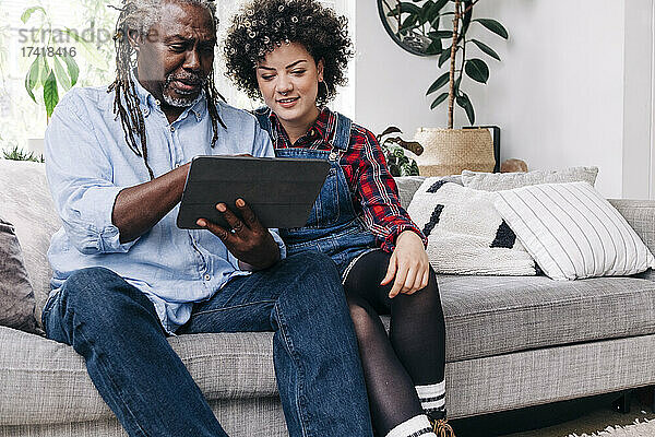 Vater und Tochter nutzen digitales Tablet  während sie auf dem Sofa sitzen