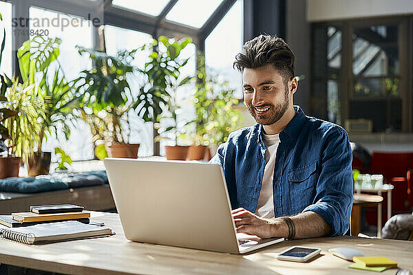 Lächelnder männlicher Profi  der am Schreibtisch im Büro am Laptop arbeitet