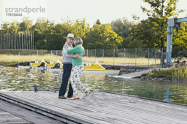 Glückliches älteres Paar tanzt auf dem Steg am See