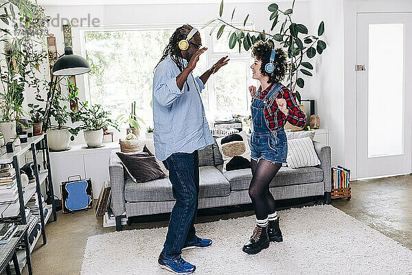 Verspielter Vater und Tochter mit Kopfhörern tanzen zu Hause