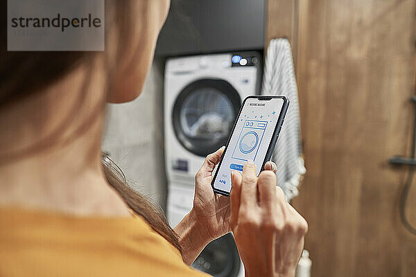 Frau bedient Waschmaschine über mobile Anwendung zu Hause