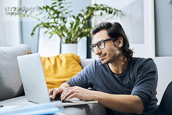 Männlicher Student mit Brille und Laptop zu Hause