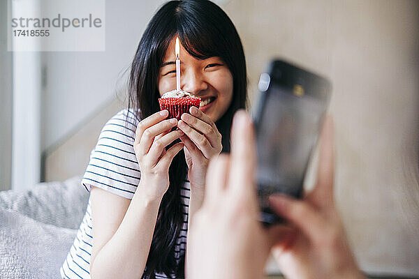 Frau fotografiert lächelnde Freundin mit Cupcake zu Hause per Handy