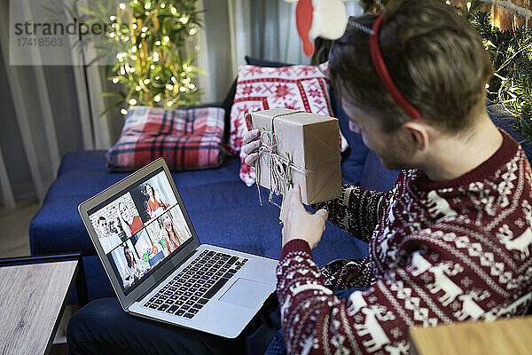 Mann zeigt Weihnachtsgeschenk während Videoanruf über Laptop zu Hause
