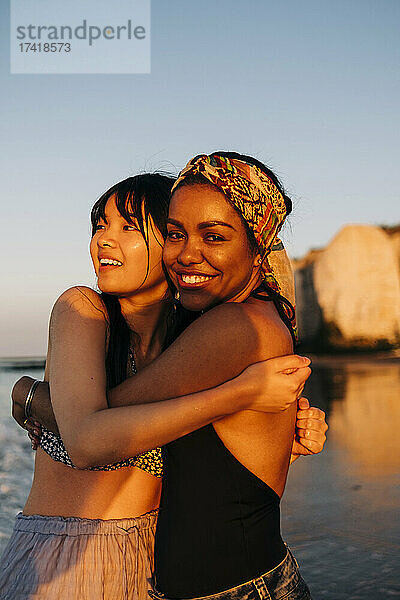 Lächelnde Freundinnen umarmen sich am Strand