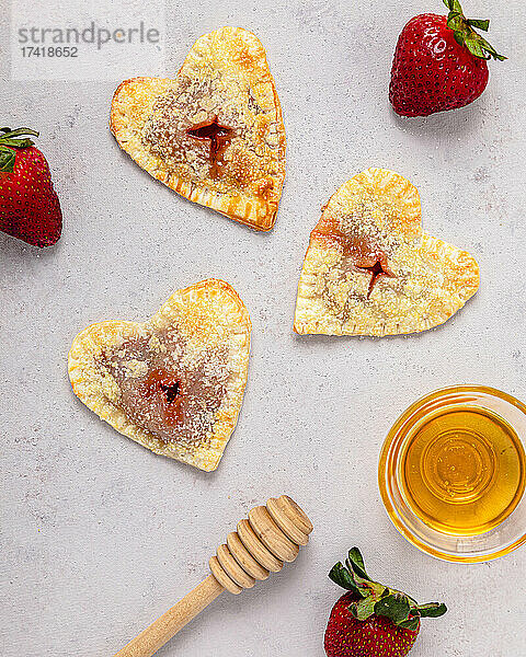 Studioaufnahme einer Schüssel Honig  Honigschöpflöffel  Erdbeeren und frisch gebackenen herzförmigen Minikuchen