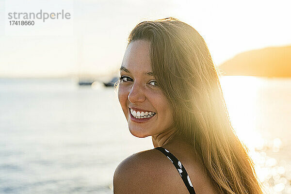 Fröhliche junge Frau blickt am Strand über die Schulter