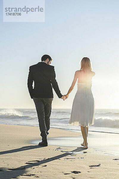 Paar hält Händchen beim Spaziergang am Strand