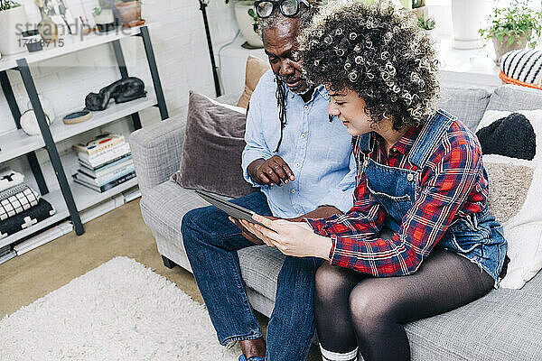 Frau benutzt digitales Tablet  während sie neben ihrem Vater auf dem Sofa sitzt
