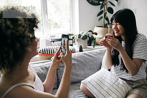 Frau fotografiert einen Freund  der zu Hause einen Cupcake über sein Mobiltelefon hält