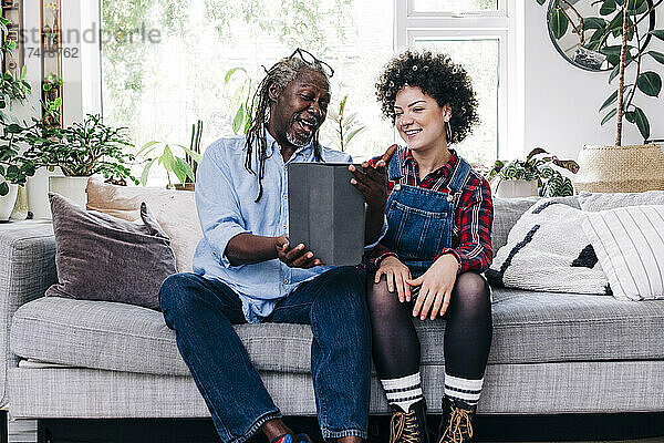 Lächelnder Vater und Tochter telefonieren per Video über ein digitales Tablet im Wohnzimmer