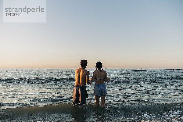 Junge männliche und weibliche Freunde blicken bei Sonnenuntergang auf das Meer
