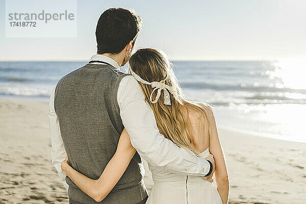 Frischvermähltes Paar steht mit dem Arm um den Strand