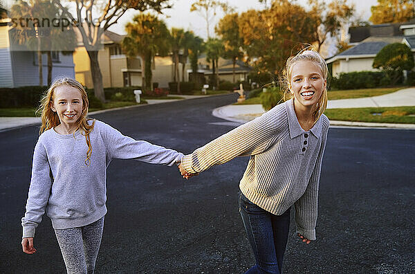 Lächelnde Mädchen halten sich beim Gehen auf der Straße an den Händen
