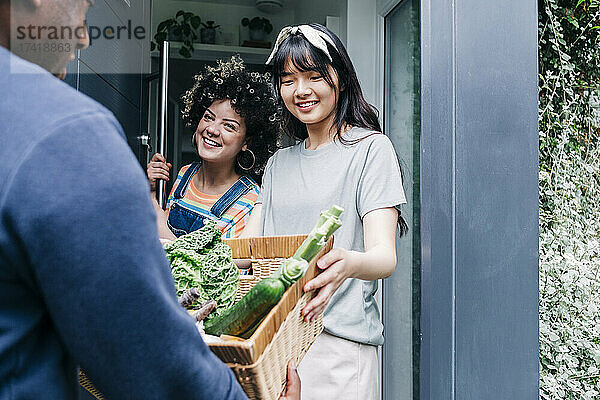 Männlicher Zusteller liefert frisches Gemüse an Frauen vor der Tür