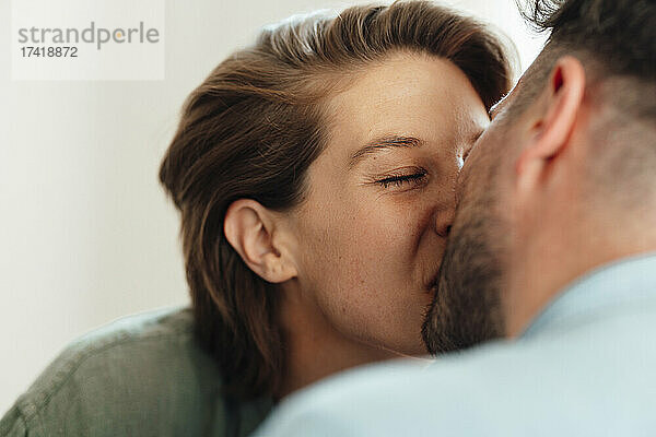 Frau mit geschlossenen Augen küsst Mann zu Hause