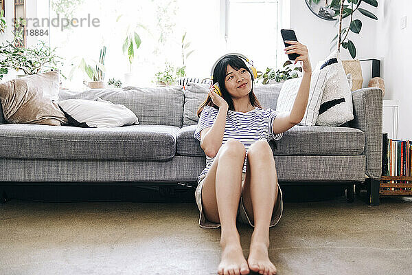 Junge Frau mit Kopfhörern macht zu Hause ein Selfie mit dem Smartphone