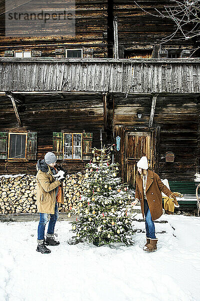 Paar schmückt den Weihnachtsbaum  während es im Schnee steht