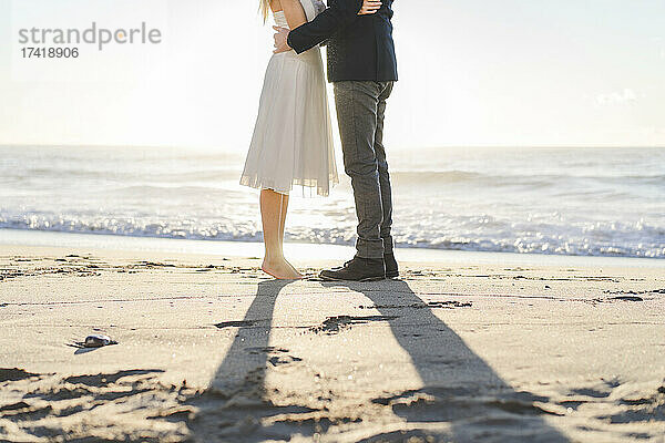 Paar umarmt sich  während es bei Sonnenaufgang am Strand steht