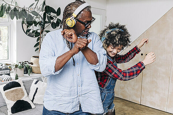 Vater und Tochter tanzen zu Hause mit Kopfhörern zusammen