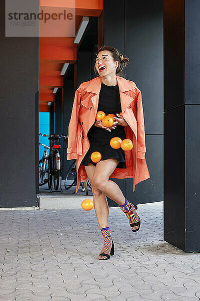 Glückliche Frau hält Orangen in der Hand  während sie auf dem Fußweg geht
