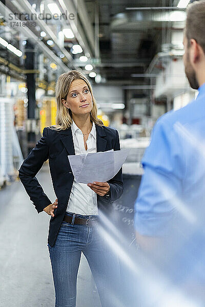 Geschäftsfrau mit Hand an der Hüfte und Blick auf Kollegin in der Fabrik