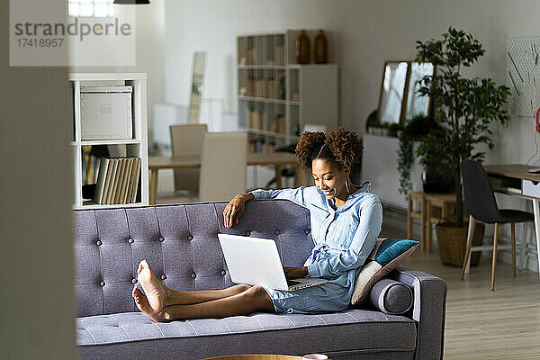 Junge Afro-Frau benutzt Laptop  während sie zu Hause auf dem Sofa sitzt