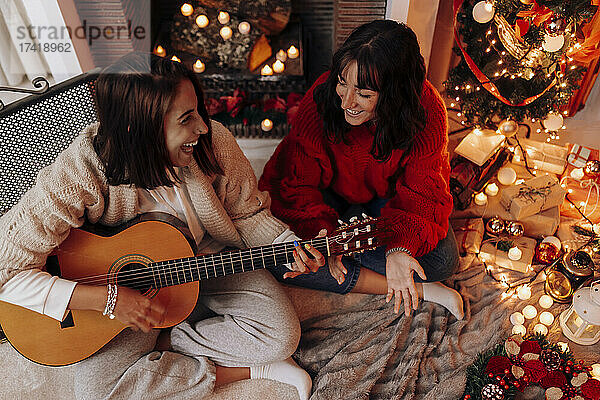 Glückliche Frau  die Gitarre spielt  während sie mit einer Freundin zu Hause sitzt