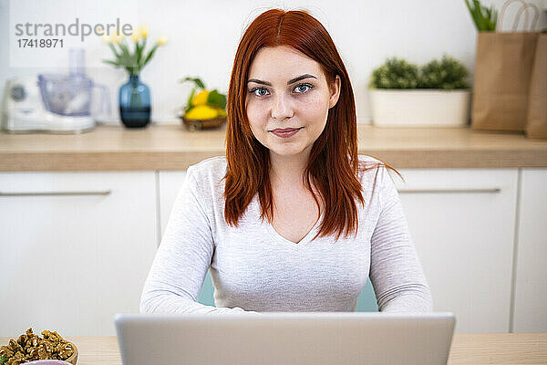 Lächelnde rothaarige Frau mit Laptop zu Hause