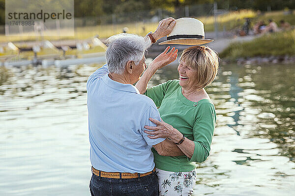 Älterer Mann setzt fröhlicher Frau am See Hut auf