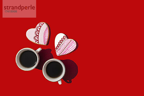 Studio shot of heart shaped cookies and two cups of coffee standing against red background