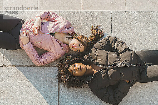 Junge Frauen in gepolsterten Jacken liegen an sonnigen Tagen auf dem Fußweg