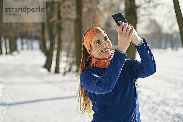 Lächelnde junge Frau  die im Winter ein Selfie mit dem Smartphone macht