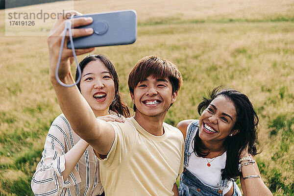 Freunde lächeln  während sie im Park ein Selfie mit dem Mobiltelefon machen