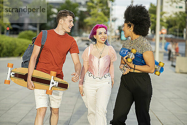 Multiethnische männliche und weibliche Freunde reden miteinander  während sie auf dem Fußweg gehen