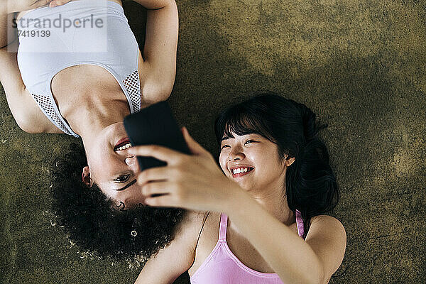 Smiling friends taking selfie through mobile phone while lying on floor