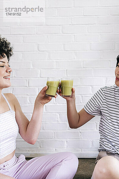 Freunde toasten Smoothie vor einer weißen Ziegelwand