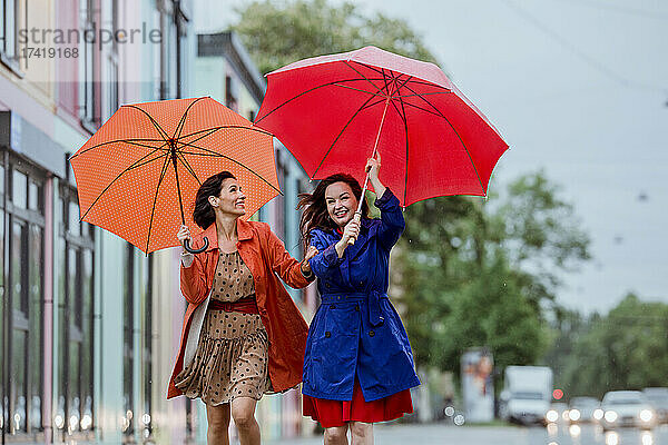 Fröhliche Freundinnen kämpfen im Regen mit Regenschirm