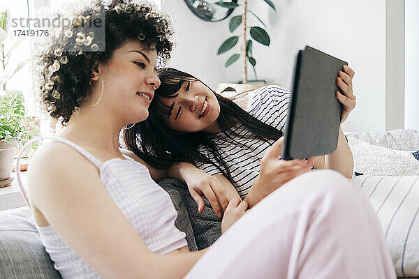 Freundinnen teilen sich ein digitales Tablet  während sie im Wohnzimmer sitzen