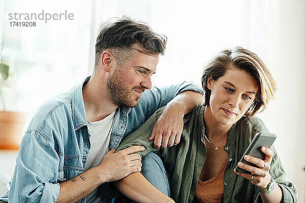 Mann sitzt neben Frau und benutzt Smartphone zu Hause