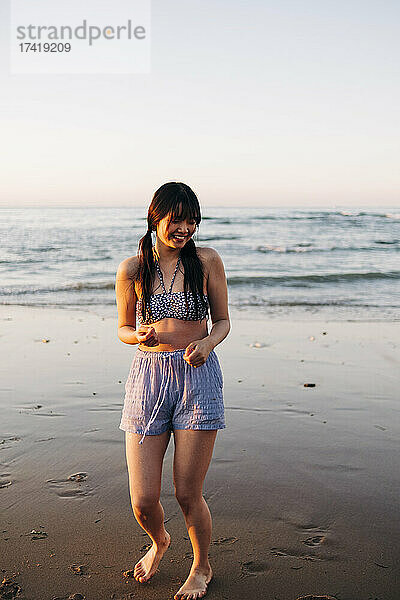 Lächelnde junge Frau  die sich bei Sonnenuntergang am Strand amüsiert