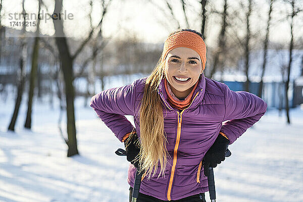 Glückliche junge Frau hält im Winter Wanderstöcke in der Hand
