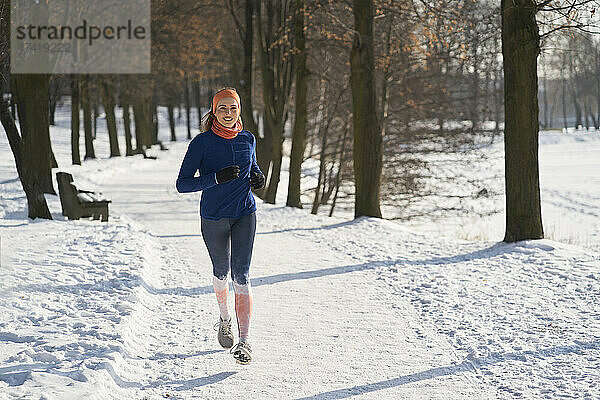 Lächelnde Frau läuft im Winter auf Schnee