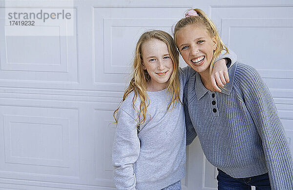 Lächelnde Mädchen mit blonden Haaren stehen vor einer weißen Wand