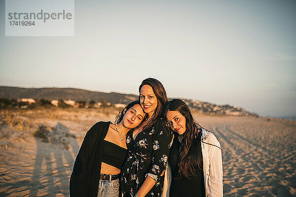 Lächelnde Töchter lehnen sich am Strand an die Schulter der Mutter