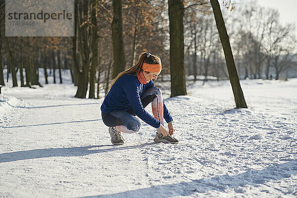 Junge Frau bindet Schnürsenkel  während sie im Winter im Schnee hockt