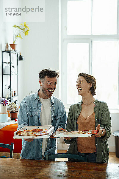 Fröhliche Männer und Frauen halten zu Hause Pizza am Tisch