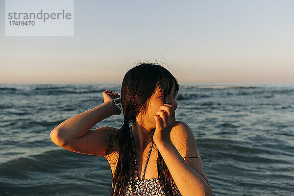 Junge Frau schaut weg  während sie bei Sonnenuntergang vor dem Meer steht