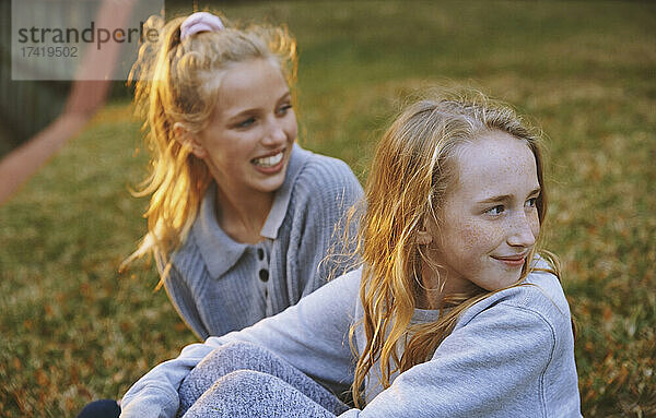 Mädchen schauen weg  während sie im Park auf Gras sitzen
